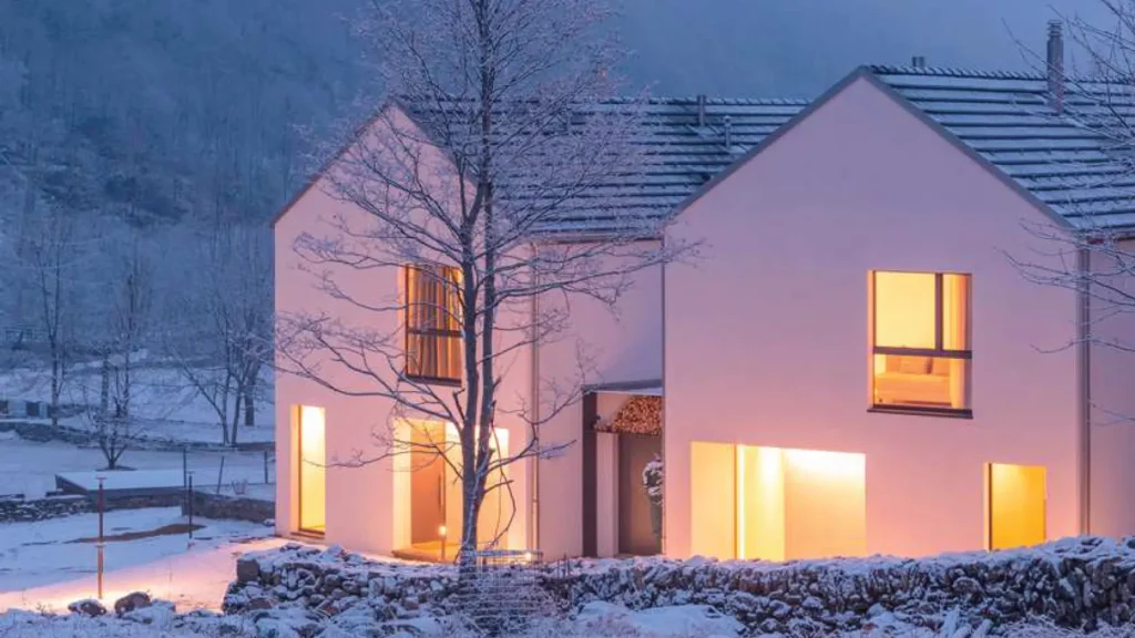 Casa moderna immersa in un paesaggio innevato al tramonto, con finestre Finstral illuminate dall’interno, simbolo di efficienza energetica e isolamento termico.